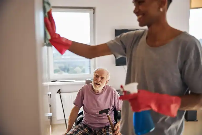 Care worker assisting an elderly man with disability in household cleaning as part of in-home support services in Adelaide