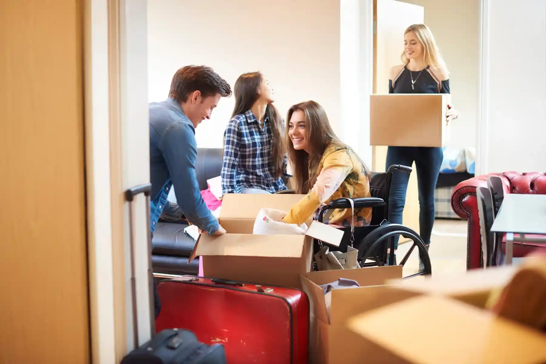 Young woman in a wheelchair smiling while unpacking boxes with friends in a shared living space.