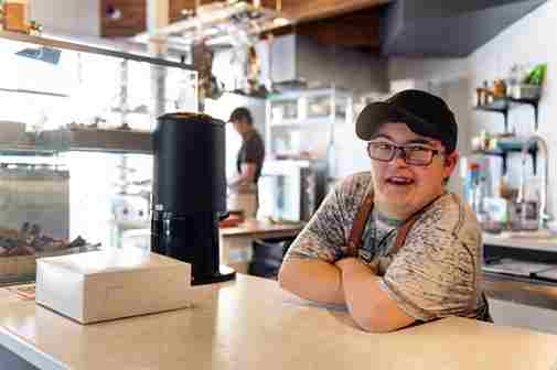 Young man with Down syndrome working at a café counter as part of supported employment services in Adelaide