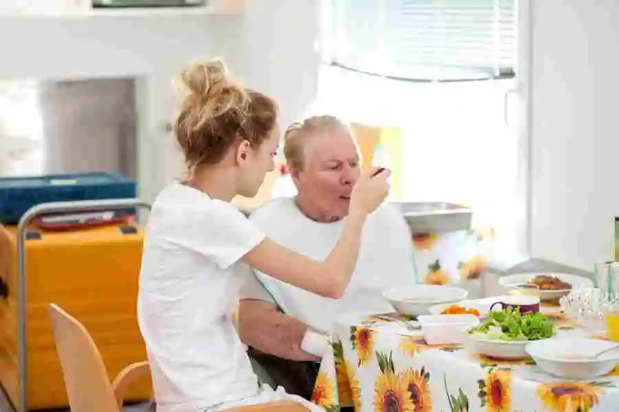 Caregiver feeding elderly woman in assisted living facility dining area in Adelaide
