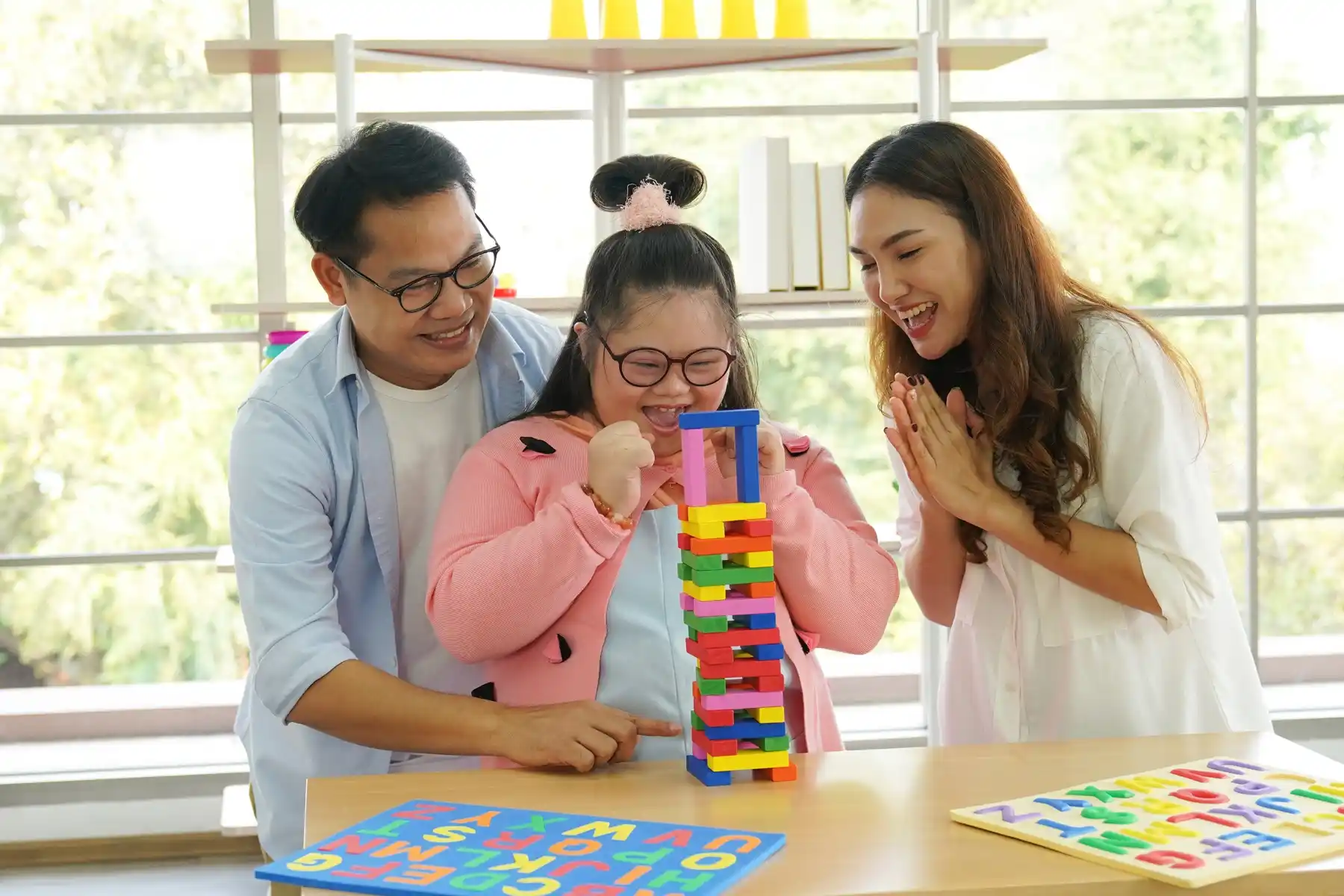 Young girl with Down syndrome participating in a cognitive development activity with two caregivers, promoting life skills and inclusive NDIS support services in a joyful educational environment.